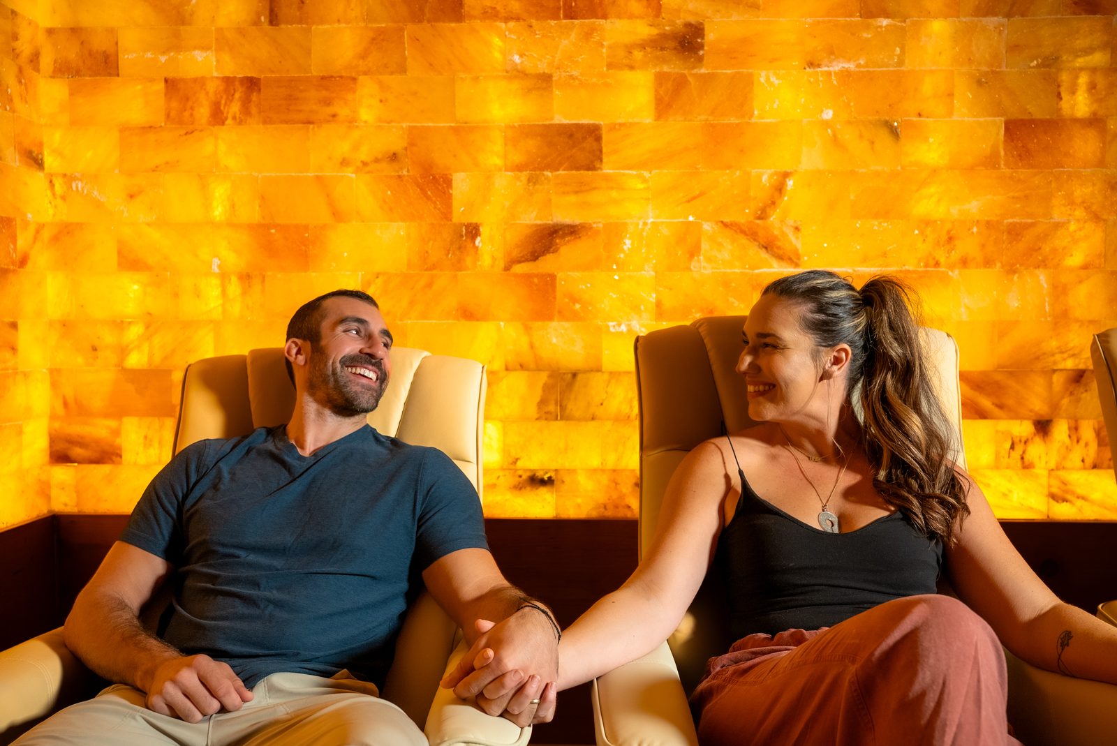 Two guests holding hands in front of the lit Himalayan salt wall